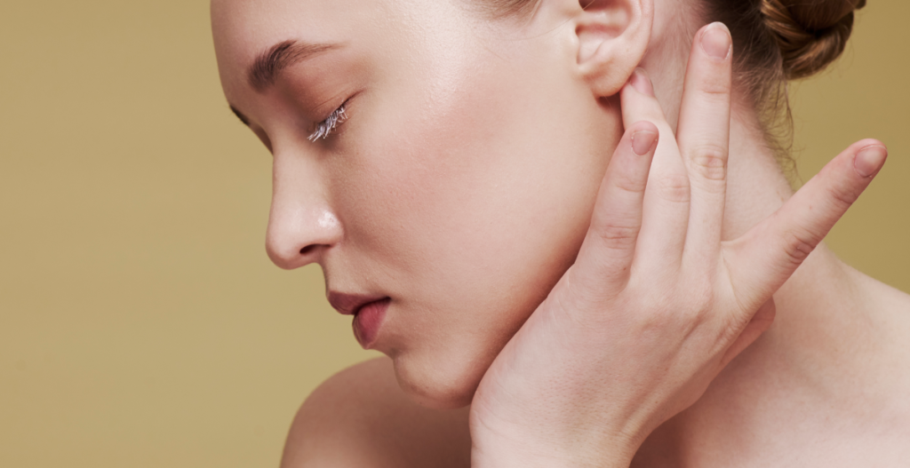 Mujer joven de perfil con piel glow, mano en el cuello, tonos durazno. Concepto: skincare realista y mitos sobre ‘la piel perfecta’ para empezar el año nuevo.