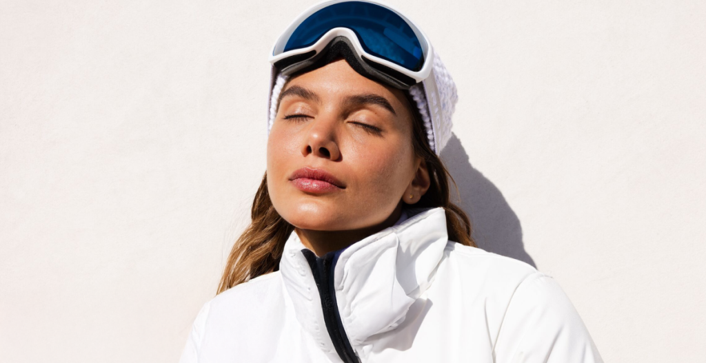 Primer plano de un rostro con protector solar aplicado, en un entorno de montaña nevada. Se aprecia el brillo intenso de la luz reflejada en la nieve, asociado a la recomendación de usar fotoprotección adecuada.