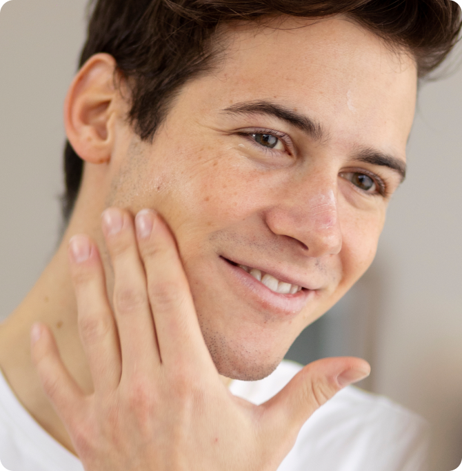 Hombre tocando su rostro con una sonrisa suave, representando el uso de productos de skincare para mantener la piel renovada e hidratada.