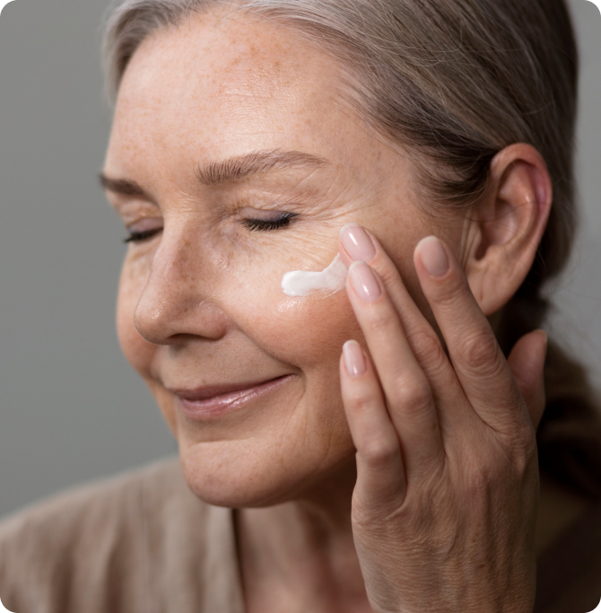 Mujer aplicando crema facial en la mejilla con expresión tranquila, mostrando una rutina de skincare enfocada en hidratación y regeneración celular.