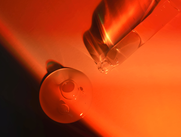 Gotero con sérum cosmético y líquido iluminado en tonos rojos, producto de cuidado facial asociado a tratamientos contra arrugas de la frente.