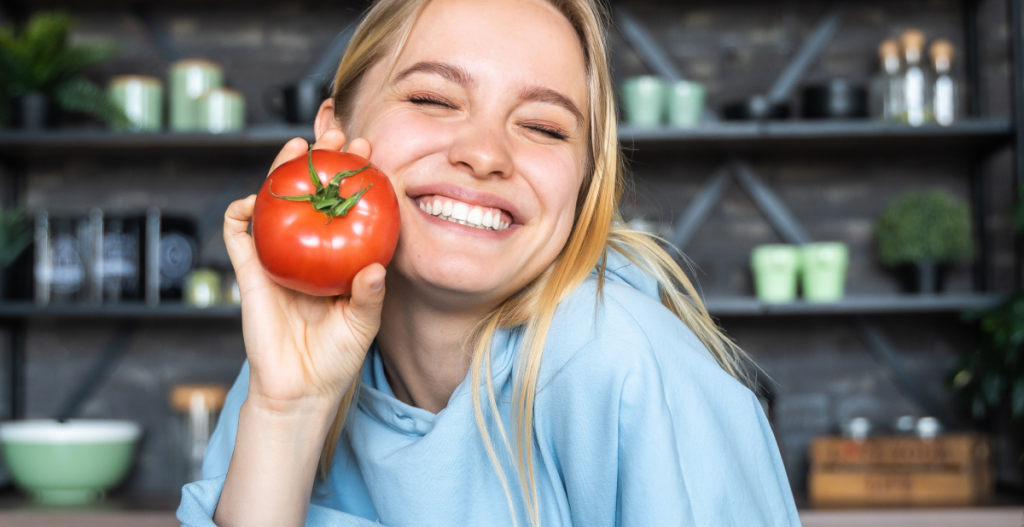 Mujer sonriendo con tomate fresco relacionado con nutrición y uñas saludables