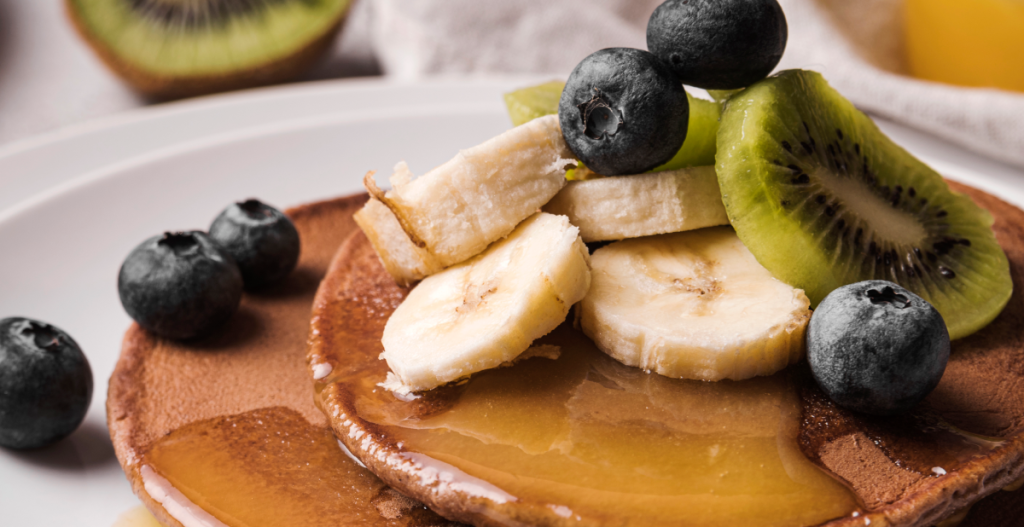 Tortitas con sirope, plátano, kiwi y arándanos, representando el consumo de azúcar relacionado con la glicación y el envejecimiento de la piel