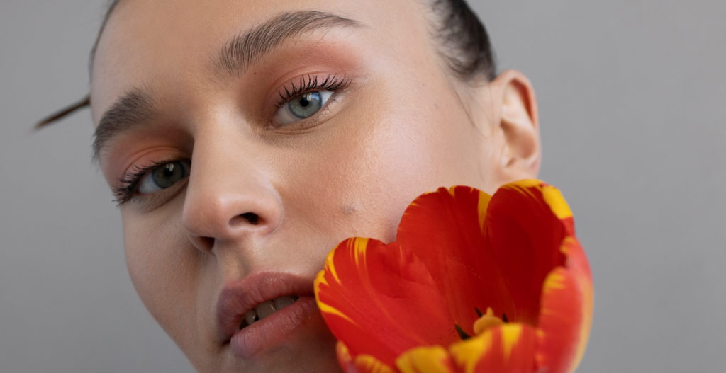 Primer plano de mujer con piel luminosa y maquillaje natural sosteniendo una flor roja, ejemplo de piel saludable en la estética make up no make up.
