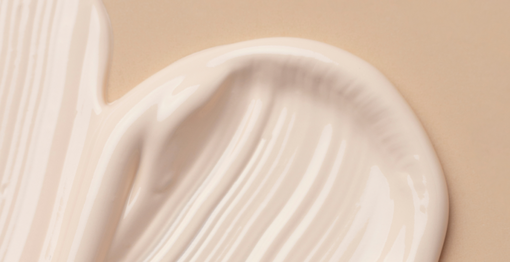 Textura cremosa blanca extendida sobre fondo beige, asociada al cuidado hidratante de la barrera cutánea.