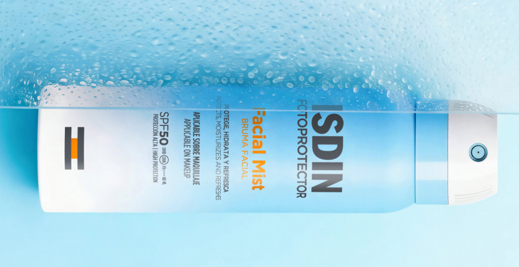 Envase de ISDIN Facial Mist SPF 50 sumergido parcialmente en agua con burbujas sobre fondo azul.
