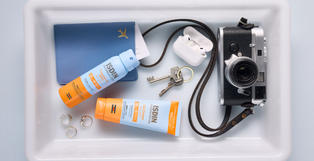Fotoprotectores ISDIN Gel Cream y Transparent Spray en una bandeja con accesorios de verano y viaje.