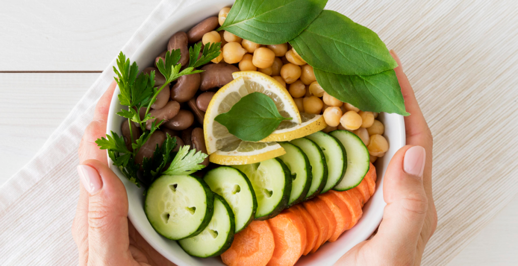 A bowl of healthy food with sliced cucumber, sweet potato, chickpeas, herbs, and lemon. Bright overhead view. Represents new healthy habits and New Year resolution goals.