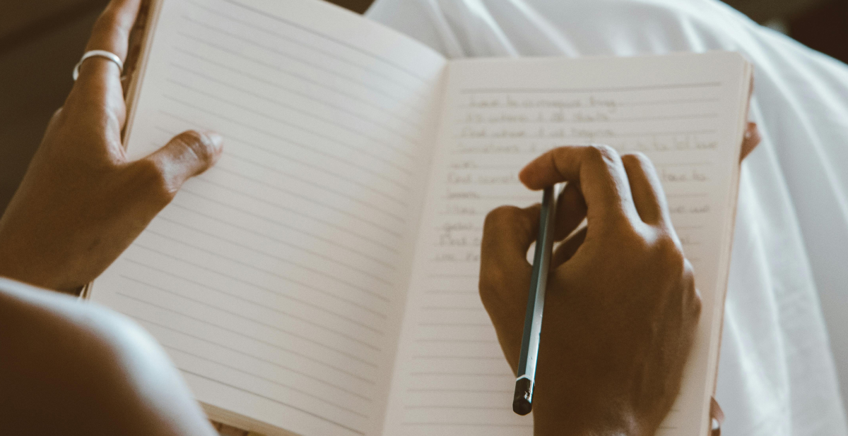 A person holding an open notebook and pen, writing goals. Warm, calm lighting. Represents setting intentions and New Year resolutions.