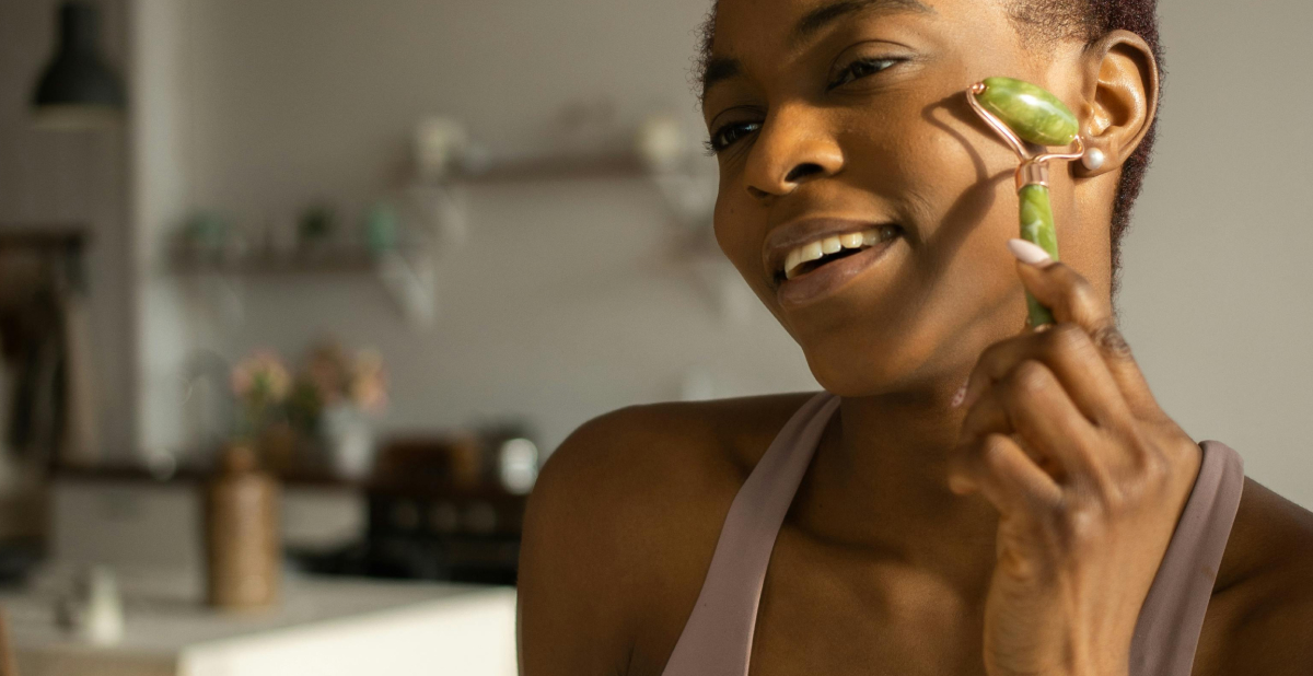 A person using a green facial roller on their cheek, soft indoor lighting, relaxed expression. Represents new skincare habits and New Year resolution self-care routines.