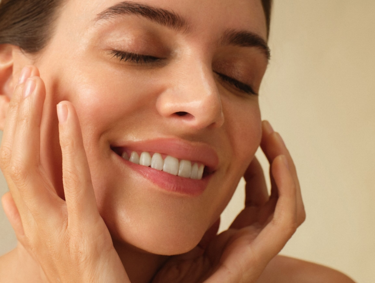 Close-up of a smiling person gently touching their face, soft blurred background, glowing skin. Represents new skincare habits and self-care for New Year resolutions.
